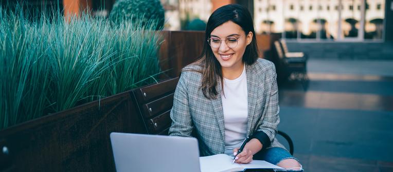 Young professional woman in blazer working on laptop outside