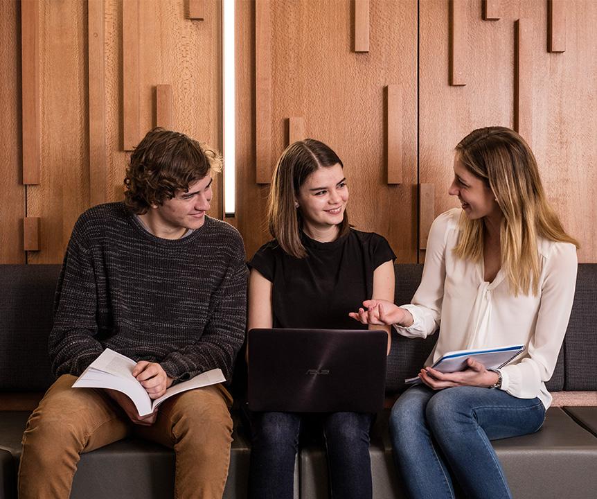 Three students sharing a laptop and chatting.