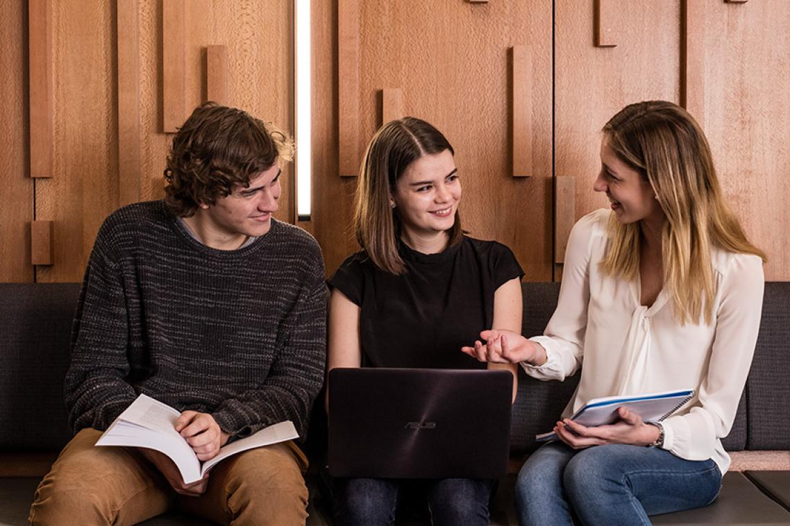 Three students sharing a laptop and chatting.